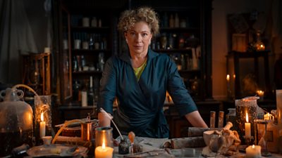 Alex Kingston leans on a table with candles and scientific materials to look like Frankenstein