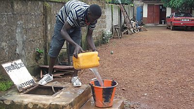A young man gets water from a chlorinated water well in Kambia, Sierra Leone