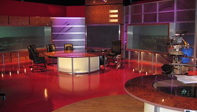 A studio with three chairs around a desk, with subdued lighting. 