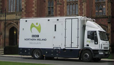 A white truck parked outside a gothic building. 