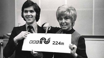 George Hamilton (left) and Gloria Hunniford (right) point at a sign saying tv R U 224M.