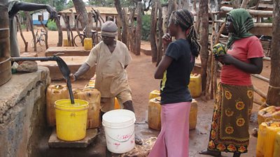 A group of villagers gather around a pump with plastic containers