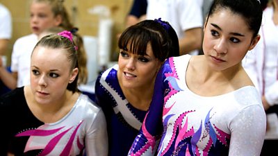 Three young female gymnasts look on nervously