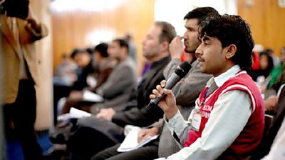 A man in an audience holding a microphone to ask a question