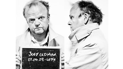 Toby Jones as Joey Oldman holding a prisoner number board