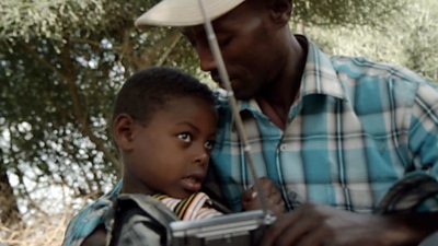 A man listening to the radio while cradling his young son