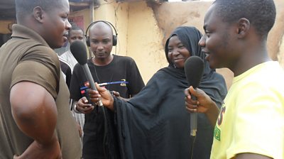 A woman and man interviewing a man while a producer looks on.