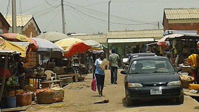 A market with brightly coloured umbrellas and a row of cars 