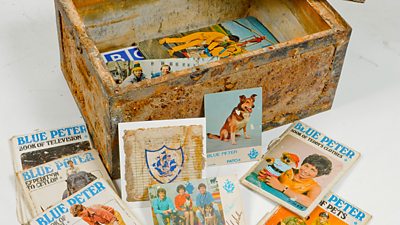 A rusty box containing various annuals, postcards and books. All are waterstained and browned. 