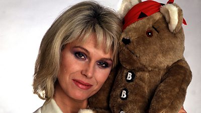 Joanna Lumley cuddles the original Pudsey mascot, which at this time is brown with a red eye patch and buttons saying B B C.