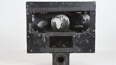 A mechanical globe sitting inside a concave mirror. These sit within a sturdy metal box. 