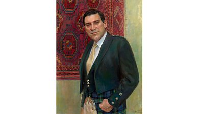 Alasdair Milne wearing a kilt, sporran with a jacket and tie. He stands looking at the painter in front of a tapestry. 