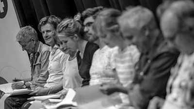 A black and white image of actors lined up with their scripts in hand.