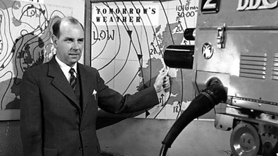 Bill Bruce points to the map, a large tv camera is pointing at him.