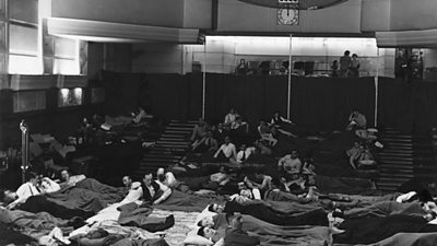 Men and women sleep on the floor of a theatre. 