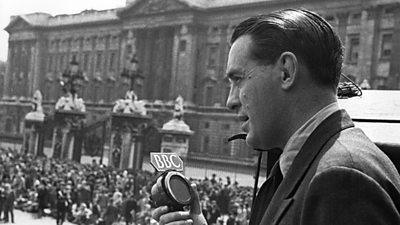 A slick-haired 鶹ҳ reporter talks into a microphone with Buckingham Palace and large crowds in the background.