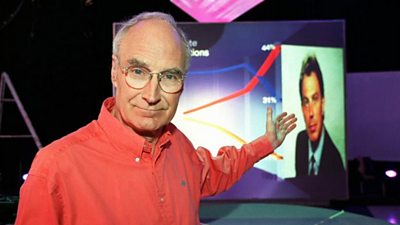 Peter Snow pointing at a large photograph of Tony Blair. He's dressed casually in an open neck shirt, in contrast to the formal suits of previous years. 