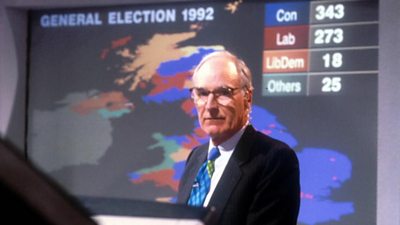 Peter Snow concentrating on a monitor. Behind him is a giant computer graphic of the UK showing the colours of wins and gains. 