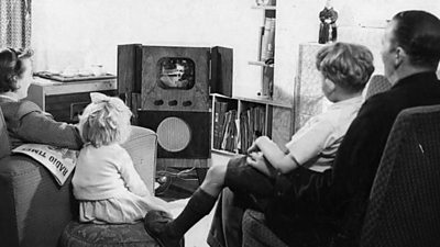 A 1950s family gathered around an old black and white television. 