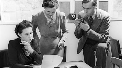 1945 election: Grace Wyndham-Goldie discusses a report with a colleagues. All are smoking cigarettes or and the man a pipe. 