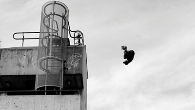 A skateboarder in the air contrasted against a brutalist industrial building