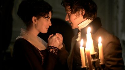 Anne Hathaway as Jane Austen looks lovingly at James McAvoy in a candle lit room. 