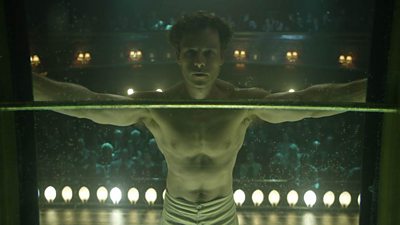 Guy Pearce as Harry Houdini suspends himself in front of a large theatre audience