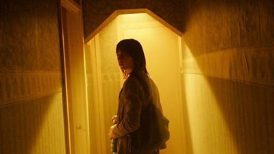 A woman stands inside a forbidding corridor