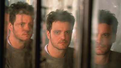 Colin Firth looking unshaven and unkempt states into a mirror, reflecting him three times