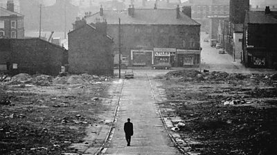 A bombed out waste ground in Liverpool, a solitary man talks along the deserted road. 