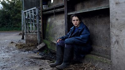 Ellie Kendrick sits alone in a muddy farmyard