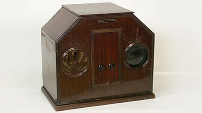 A mahogany case with two circles - one is a speaker, the other a tiny television screen. 