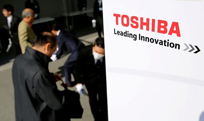 Businessmen stand beside a sign reading 'Toshiba - Leading Innovation'