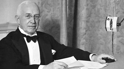 J H Whitley at a microphone wearing full black tie evening dress.
