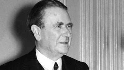 Lord Simon of Wythenshawe standing by a curtain