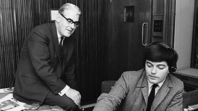 Robin Scott sits casually on the desk while Tony Blackburn spins a record in the studio