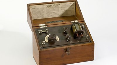 An antique crystal radio in a wooden box, a with tuning knob and an exposed valve.