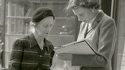 A woman with a clipboard talks to a slightly older woman. 