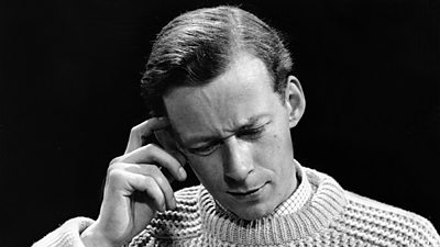 Roger Moffat in a large cable knit jumper looks at his script with a slightly forlorn expression