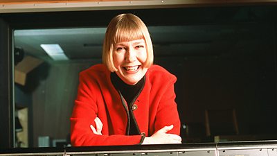 Charlotte Green in very bright red jacket cheerfully at her continuity desk