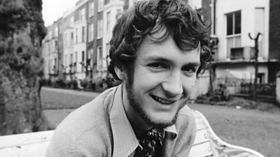 Kenny Everett in a London street. He is wearing a cravatt. 