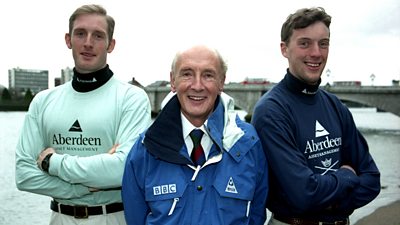 Barry Davies, in a ý jacket, stands between two very tall young men in light blue (Cambridge) and dark blue (Oxford)