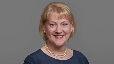 A woman with yellow hair. She is wearing a blue dress and a pearl necklace.