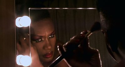 Grace Jones looks scarily at her reflection in a makeup mirror