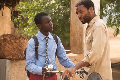 A black teenager talks to an older man holding a bicycle. 