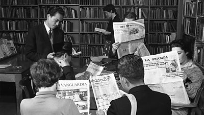 A slightly posed photograph of men and women of different nationalities reading newspapers in different languages. Titles include Die Welt, La Stampa, La Vanguardia. 