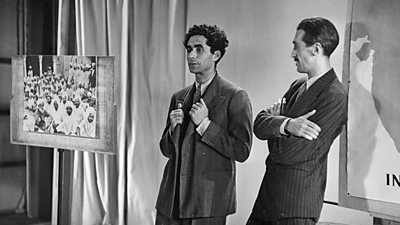 Z.A. Bokhari is interviewed by Lionel Fielden. A large photograph showing Indians in traditional dress is on an easel. 