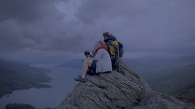 A group sit at the top of a mountain overlooking a loch