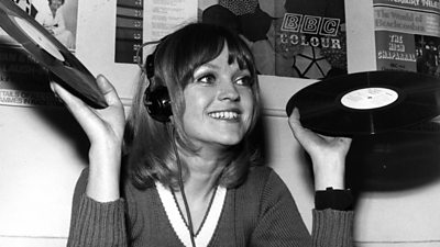 A young Annie Nightingale wearing headphones and holding two records.