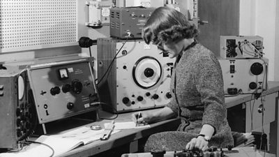 A woman turns the dial on a complex setup of audio equipment.